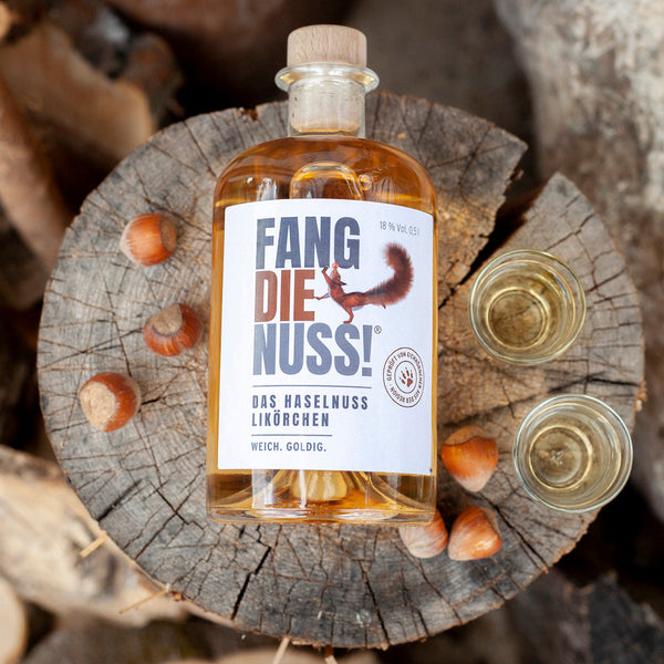 fang die nuss haselnusslikör flasche 500ml auf baumstamm mit haselnüssen und gläser